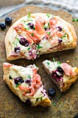 Pizza with goat's cream cheese, ham and blueberries