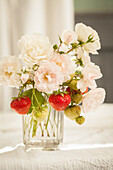 Summer bouquet of white garden roses and sprigs of strawberries in glass vase
