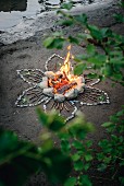 Romantisches Lagerfeuer an Flussufer mit Blumenmotiv aus Steinen und Stöckchen
