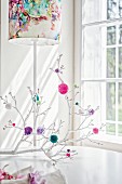 White branches decorated with colourful pompoms decorating table in front of standard lamp with colourful lampshade