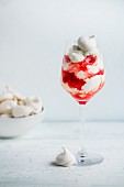 A creamy dessert with berry sauce topped with meringue in a stemmed glass