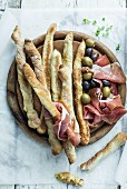 Grissini with ham and olives on a wooden board (seen from above)