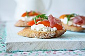 Bruschetta with goats' cheese, almonds, tomato slices, cured ham and rocket