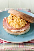 An English muffin topped with scrambled eggs and ham