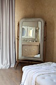 Cheval mirror seen across button-tufted couch in corner of Mediterranean room