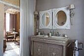 Elegant washstand with twin inset sinks below round mirrors next to curtain in doorway