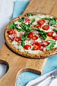 A pizza with ham, spinach and tomatoes