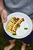 A man holding a plate of grilled pineapple and quark cream