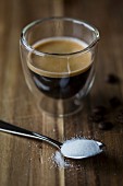 Ein Espresso im Glas davor Kaffeelöffel mit Zucker