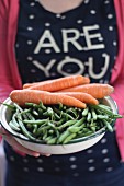 A woman holding a bowl of green beans and carrots
