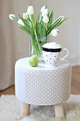 Cup of cappuccino and vase of white tulips on grey polka-dot stool