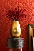 Twigs of red berries in gold vase on fur-covered stool