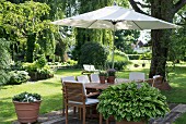 Parasol integrated in garden table and wooden chairs with white cushions in summer garden