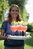 Cheerful woman serving tray of drinks in garden