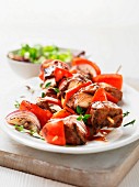 Barbecued meat skewers with red onions, peppers and herbs