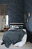 Bed with grey blanket and white bed linen in corner of masculine room with floral wallpaper