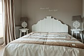 Doppelbett mit weißem, verziertem Holzbettkopfteil vor taupefarbener Wand in elegantem Schlafzimmer