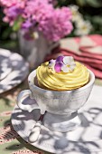 A cupcake decorated with vanilla cream and pansies on garden table