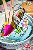 Vintage-style painted enamel colander and spatulas in bowl on garden table in sunshine