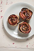 Three shortcrust apple roses on a white plate with icing sugar