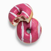 Two pink strawberry doughnuts filled with strawberry jam, one with a bite taken out