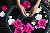 Schwimmende Rosenblüten und Teelichter in Keramikschale, Mädchenhände halten pinkfarbene Blüte