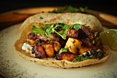A taco filled with pork belly, grilled fruit and coriander