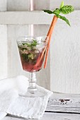 A rhubarb drink with ice cubes and mint in a glass, garnished with a rhubarb stick
