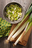 Whole leeks on a chopping board and sliced leeks in a colander