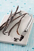 Vanilla pods and a knife with vanilla seeds on a chopping board