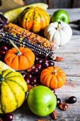 Pumpkins, corn cobs, apples, nuts and cranberries on a wooden surface