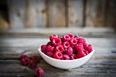 A bowl of fresh raspberries on a rustic wooden surface