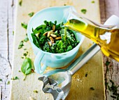 Olivenöl zur Basilikum-Pinienkern-Mischung geben