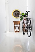 Weisser Gang mit glänzendem Boden und an Wand aufgehängtem Fahrrad, moderner Holzstuhl im Hintergrund