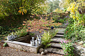 Watering cans on edge of pond and steps in autumnal garden