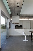 Modernes Wohnhaus mit offener Küche und weißem Klassiker Schalenstuhl, oberhalb eingelassene Strahler in Sichtbetonunterzug