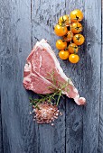 A fresh veal chop, salt, rosemary and yellow tomatoes on wooden surface