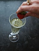 A woman placing a strawberry in a glass of prosecco
