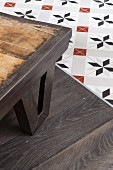Corner of table with metal frame and metal frame on parquet floor adjoining ornamental floor tiles