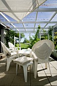 White plastic chairs and stools with seat cushions below awning in conservatory