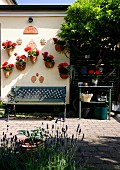 Hängende Blumentöpfe an Hauswand, Gartenbank