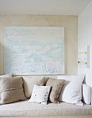 White and ecru cushions on bench below modern artwork on wall