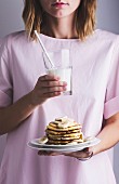 A girl holding a plate of pancakes and bananas, and a glass of milk