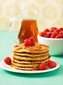 A stack of pancakes with raspberries and maple syrup