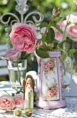 Vintage-style arrangement of roses, rose-patterned coffee jug and angel on table