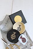 Hand-made foam rubber pineapple stamp, box with stamped motif and printed picture with golden circle lying on grey cloth