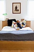 Double bed with headboard, geometrically patterned scatter cushions and checked bedspread below framed vintage photo of child on wall