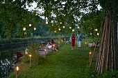 Partystimmung im Garten, Gäste zwischen Fackelleuchten und Lampions an Baumzweigen