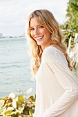 A young blonde woman wearing a light, oversized top by the sea