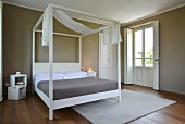 White four-poster bed with canopy in elegant bedroom with dark walls